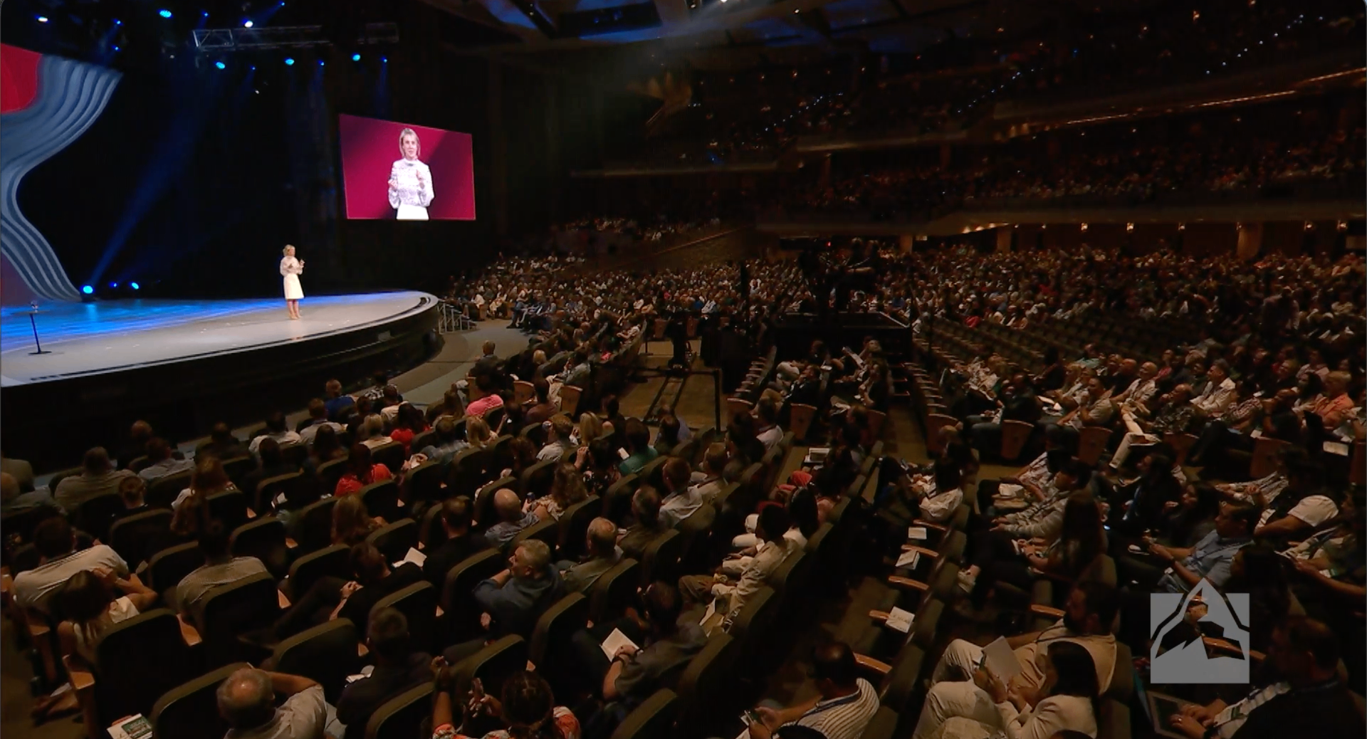 Sahar Hashemi speaking on a large stage to a packed auditorium